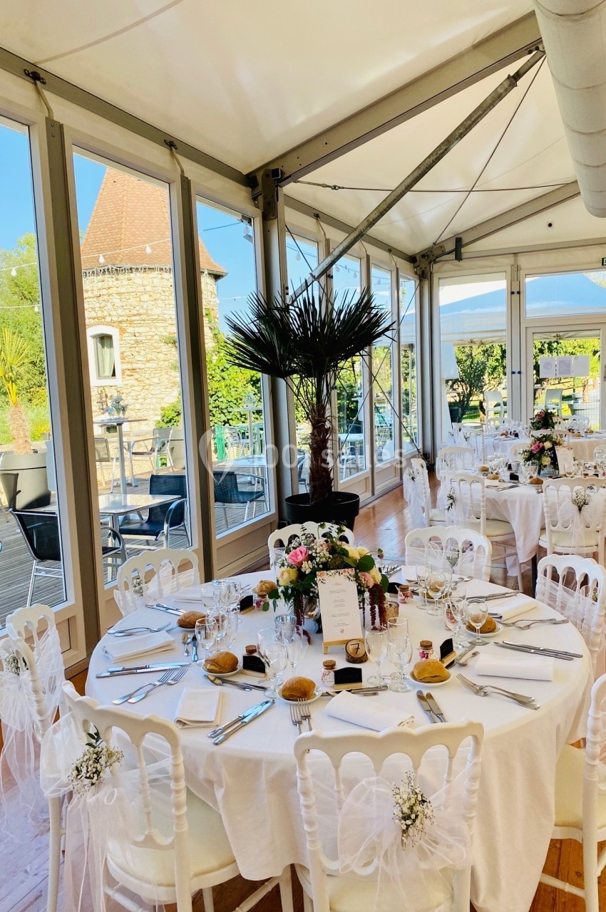 Location salle Vignieu (Isère) - Domaine de Suzel #55 Salle de réception lumineuse avec tables rondes décorées pour un événement, vue sur une terrasse et un jardin.