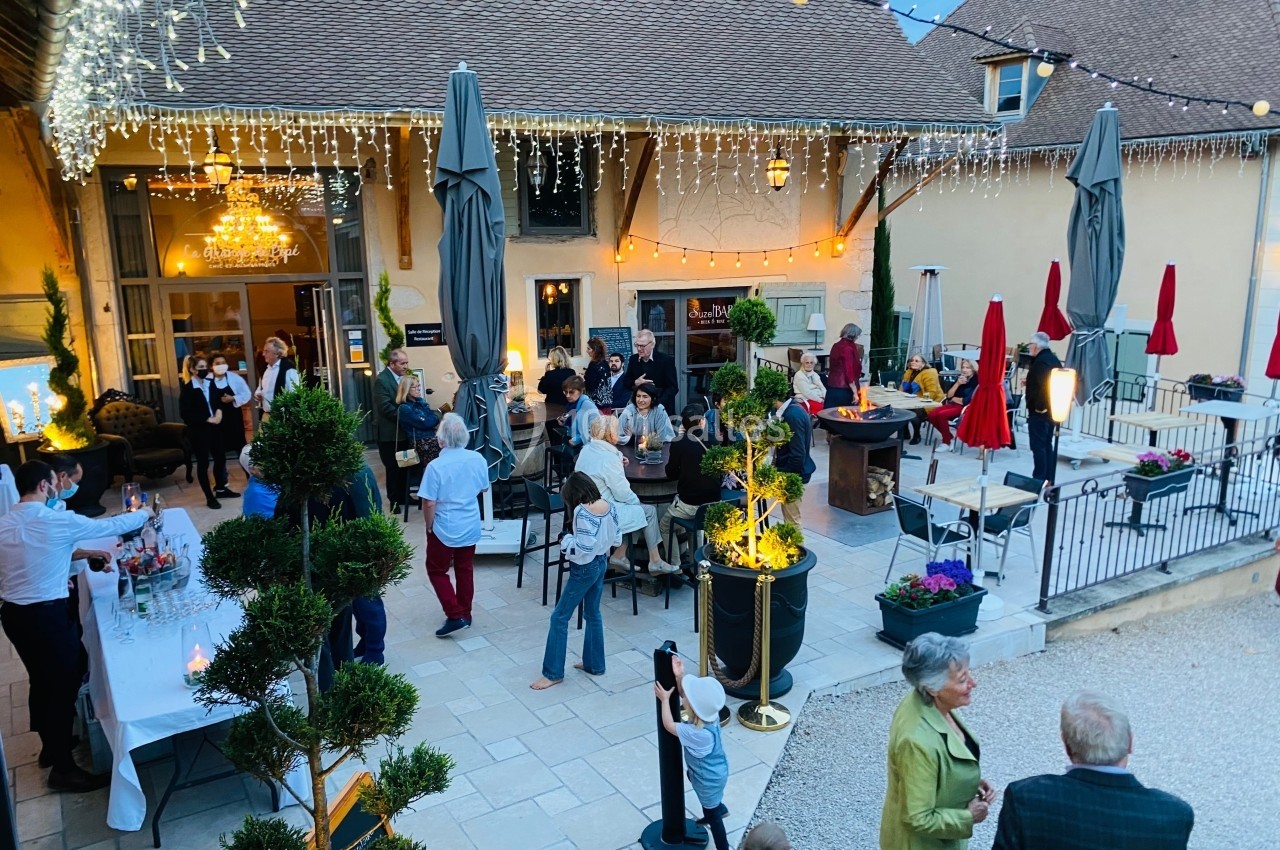 Location salle Vignieu (Isère) - Domaine de Suzel #56 Groupe de personnes réunies dans une cour extérieure décorée de guirlandes lumineuses, en soirée.