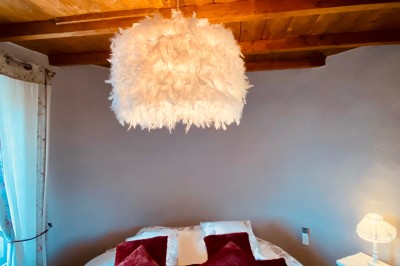 Miniature Location salle Vignieu (Isère) - Domaine de Suzel #60 Chambre avec lit rond, couverture rouge, pétales de rose, lampe de chevet et plafond en bois avec suspension plumeuse.