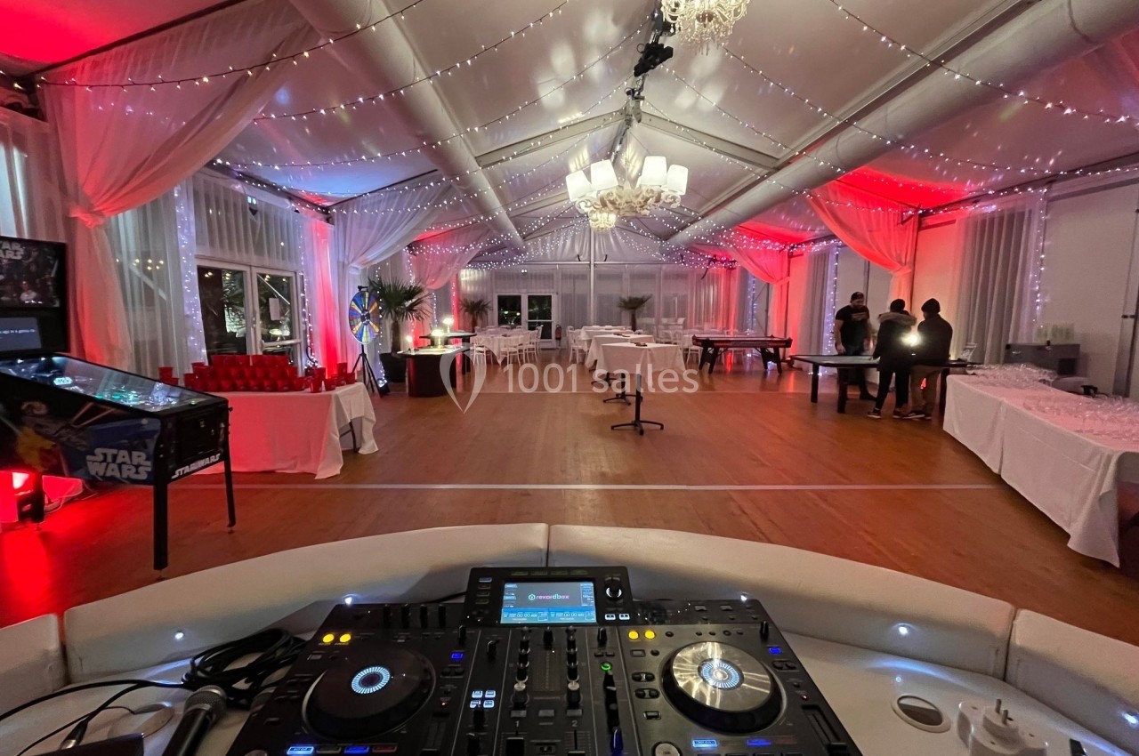 Salle de réception décorée avec des guirlandes lumineuses, vue depuis une table de mixage au premier plan.