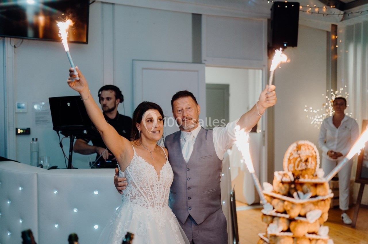 Un couple en tenue de mariage tient des cierges magiques allumés lors d'une réception festive.