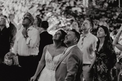 Un couple de dos regarde un feu d'artifice illuminer le ciel nocturne dans un cadre extérieur.