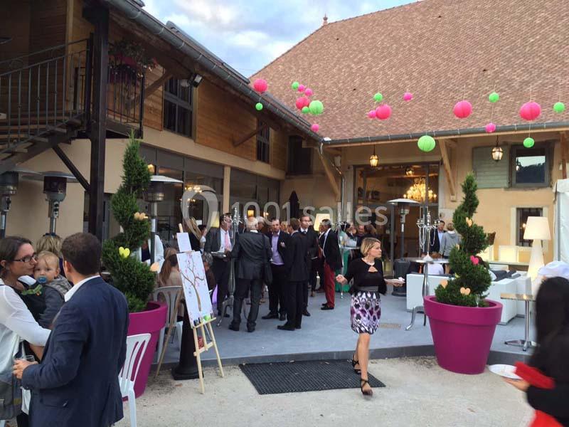 Location salle Vignieu (Isère) - Domaine de Suzel #16 Groupe de personnes réunies dans une cour extérieure décorée de lanternes colorées, près d'un bâtiment en bois.