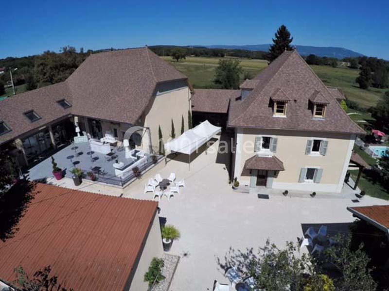Location salle Vignieu (Isère) - Domaine de Suzel #5 Vue aérienne d'un bâtiment avec toits en tuiles, une terrasse aménagée et un espace extérieur dégagé.