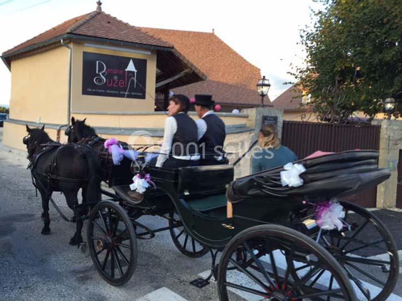 Location salle Vignieu (Isère) - Domaine de Suzel #17 Une calèche tirée par deux chevaux passe devant un bâtiment beige avec un panneau indiquant ’Brasserie Suzel’.