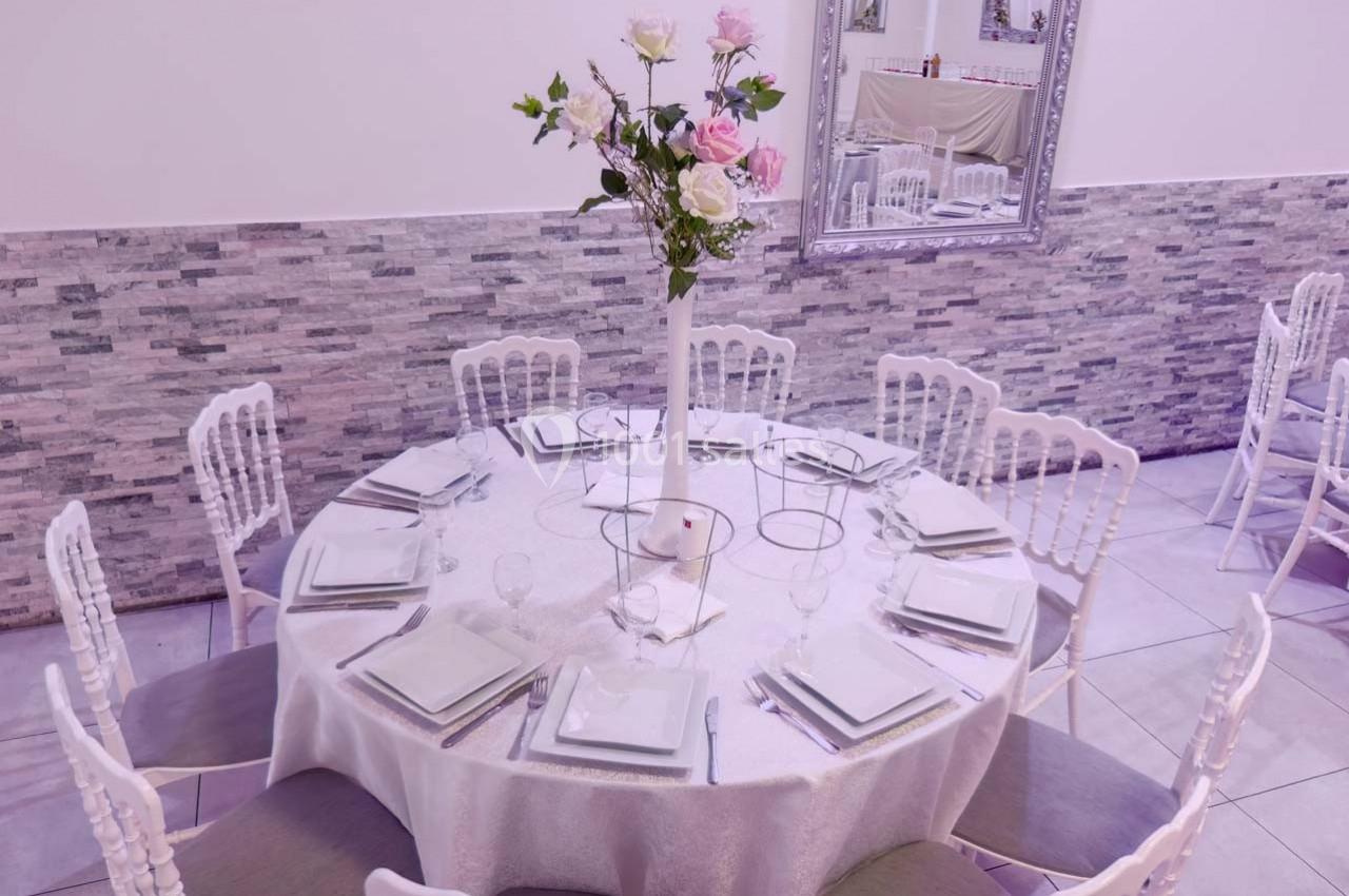 Table ronde élégamment dressée avec nappes blanches, assiettes carrées et un centre de table floral.