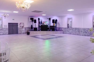 Salle de réception spacieuse avec piste de danse, éclairages colorés et équipement audio sur une estrade.