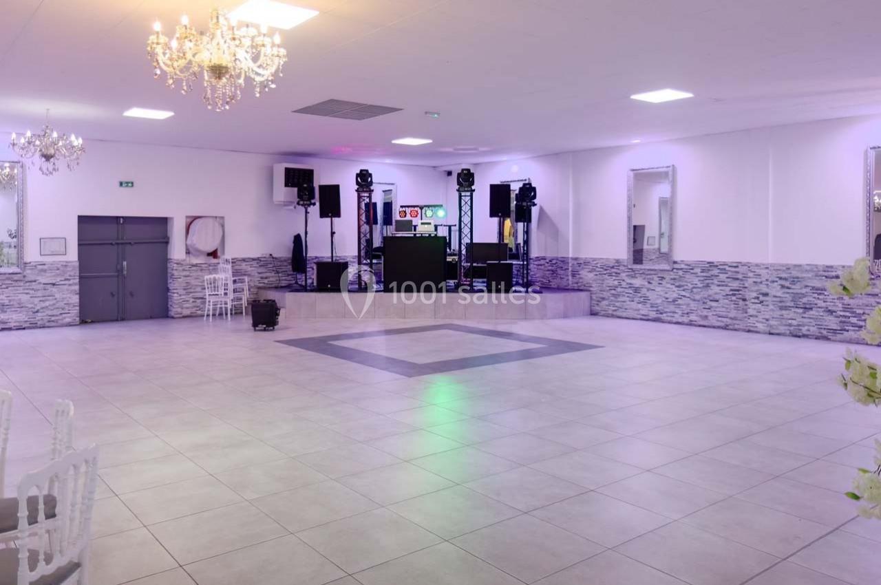 Salle de réception spacieuse avec piste de danse, éclairages colorés et équipement audio sur une estrade.