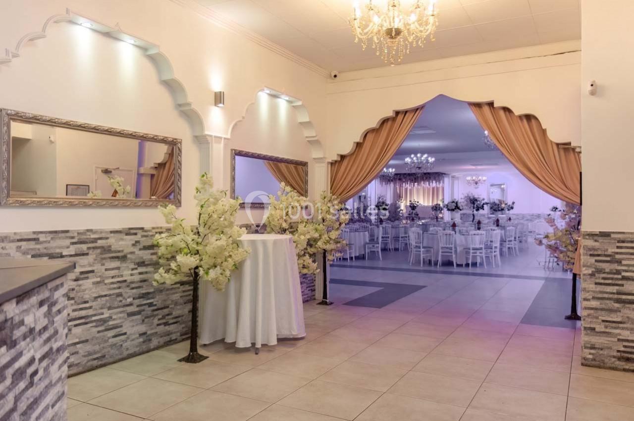 Salle de réception élégante avec rideaux dorés, lustres et tables décorées visibles en arrière-plan.