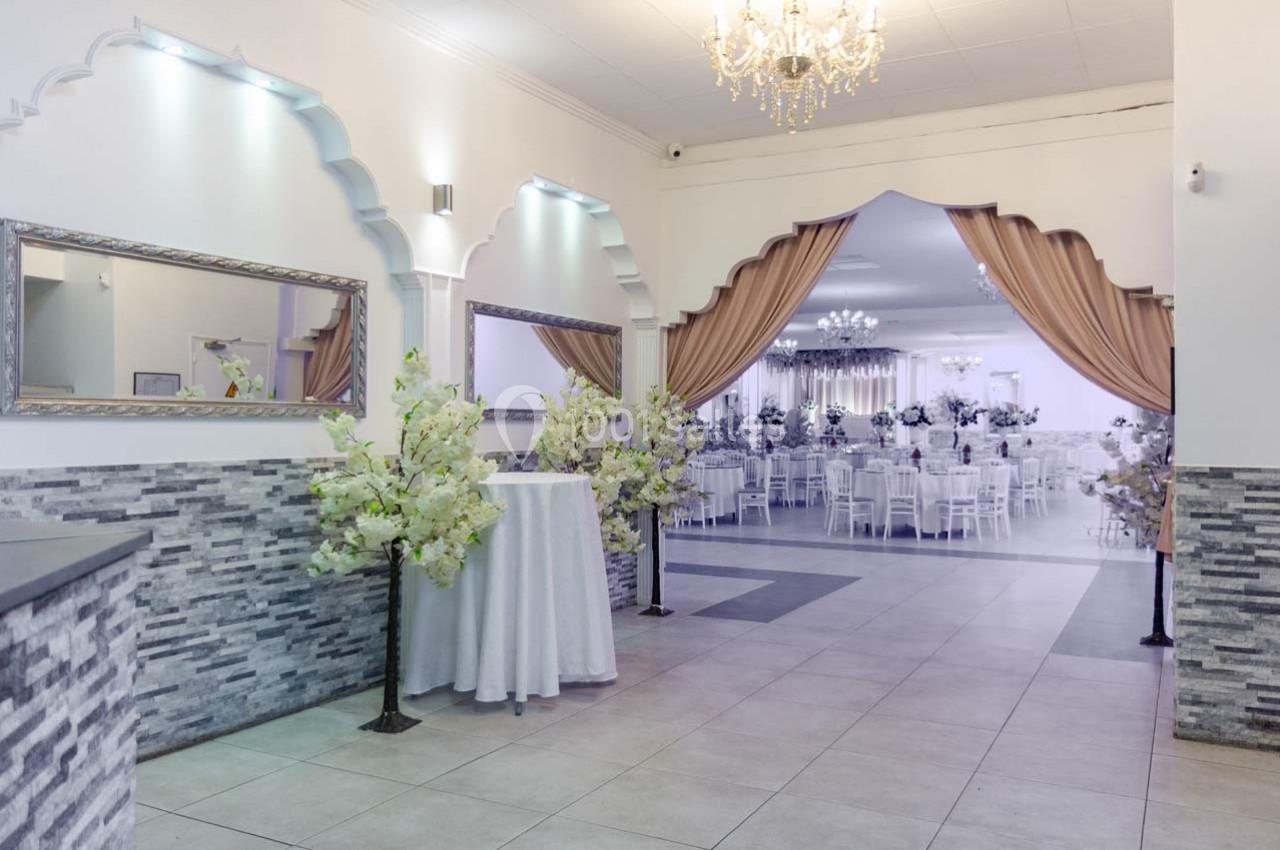 Salle de réception élégante avec décor floral, tables dressées et rideaux encadrant l'entrée vers l'espace principal.