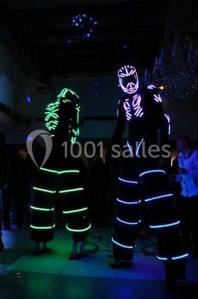 Location salle Vignieu (Isère) - Domaine de Suzel #13 Deux personnes sur échasses portent des costumes lumineux avec des motifs fluorescents dans une ambiance sombre.