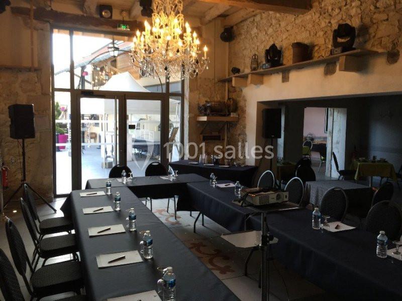 Location salle Vignieu (Isère) - Domaine de Suzel #3 Salle de réunion lumineuse avec tables disposées en U, chaises, projecteur et vue sur une terrasse extérieure.