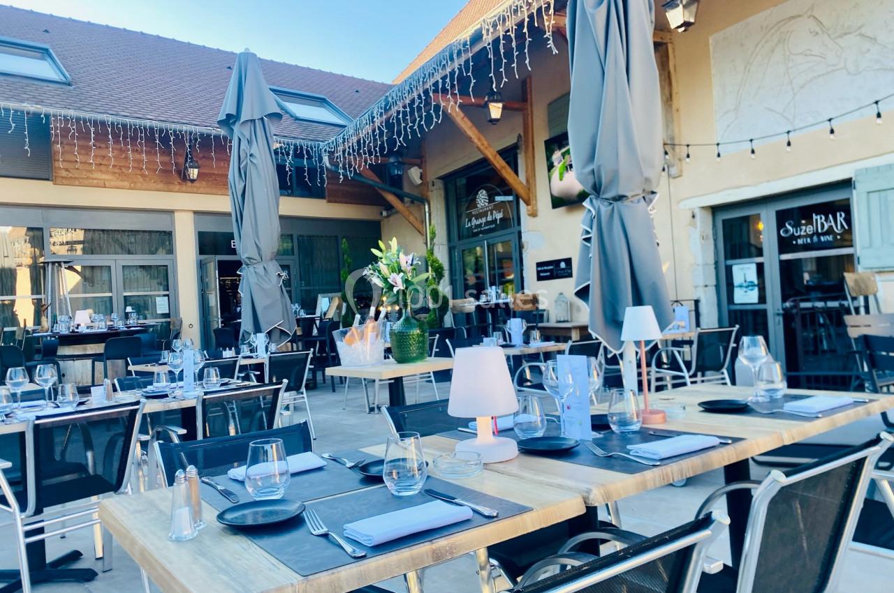 Location salle Vignieu (Isère) - Domaine de Suzel #18 Terrasse d'un restaurant avec tables dressées, parasols gris, décoration florale et éclairage suspendu.