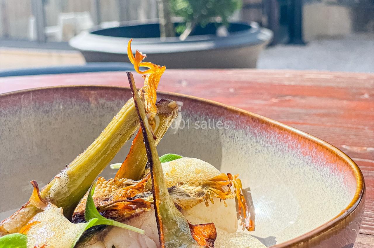 Location salle Vignieu (Isère) - Domaine de Suzel #21 Assiette en céramique contenant un plat garni de légumes grillés, posée sur une table en bois en extérieur.