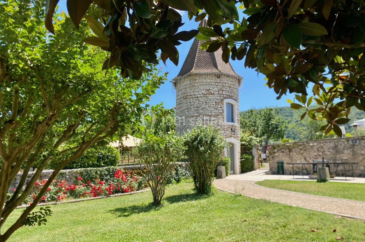 Location salle Vignieu (Isère) - Domaine de Suzel #37 Tour en pierre entourée de verdure, avec des arbres, des fleurs et un chemin dans un jardin ensoleillé.