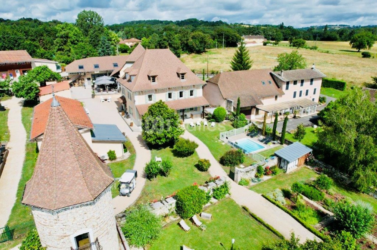 Vue aérienne d'un domaine avec plusieurs bâtiments en pierre, une piscine, des jardins et des espaces verts environnants.
