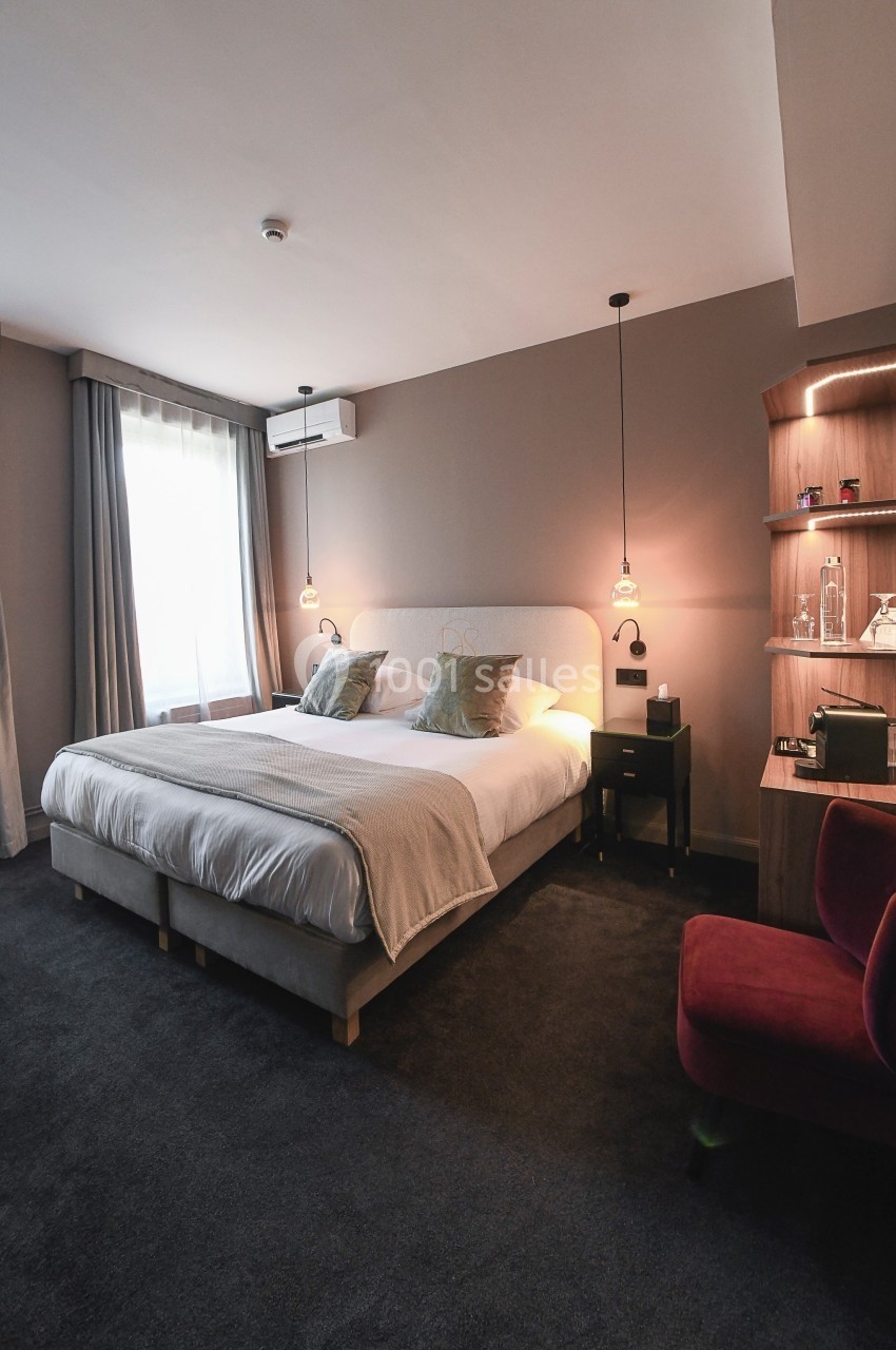 Location salle Vignieu (Isère) - Domaine de Suzel #40 Chambre d'hôtel moderne avec un grand lit double, éclairage suspendu, fauteuil rouge et étagères en bois.