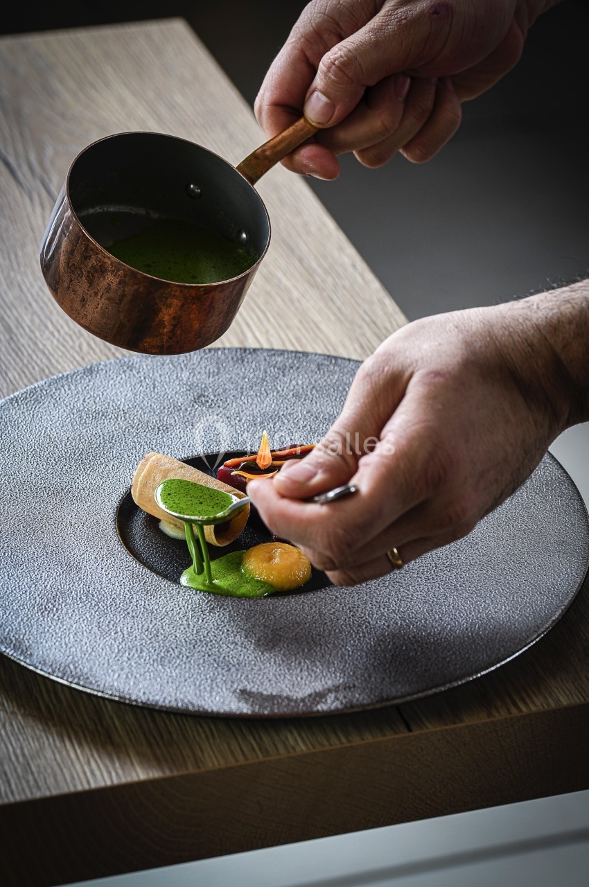 Location salle Vignieu (Isère) - Domaine de Suzel #41 Un chef verse une sauce verte sur un plat raffiné présenté sur une assiette grise texturée.