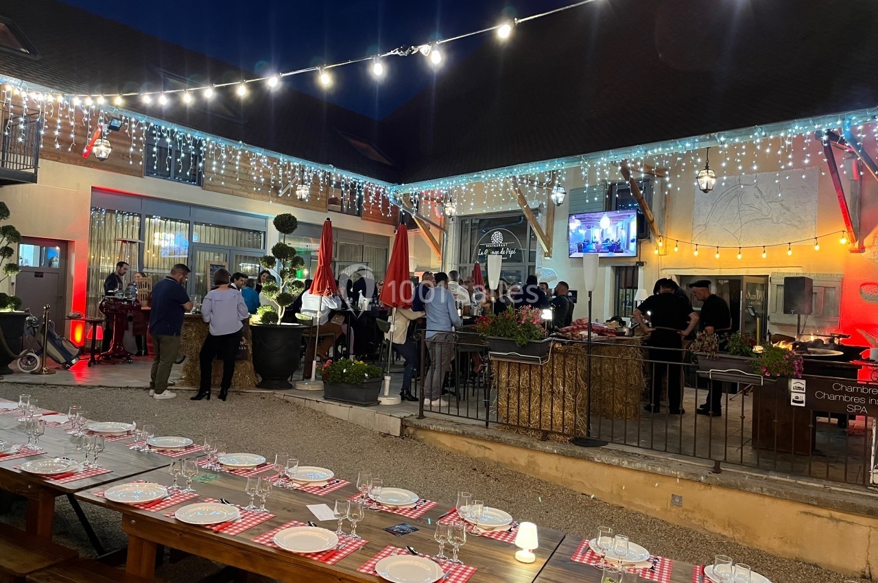 Location salle Vignieu (Isère) - Domaine de Suzel #43 Cour extérieure éclairée en soirée avec des tables dressées, des invités debout et un buffet en arrière-plan.
