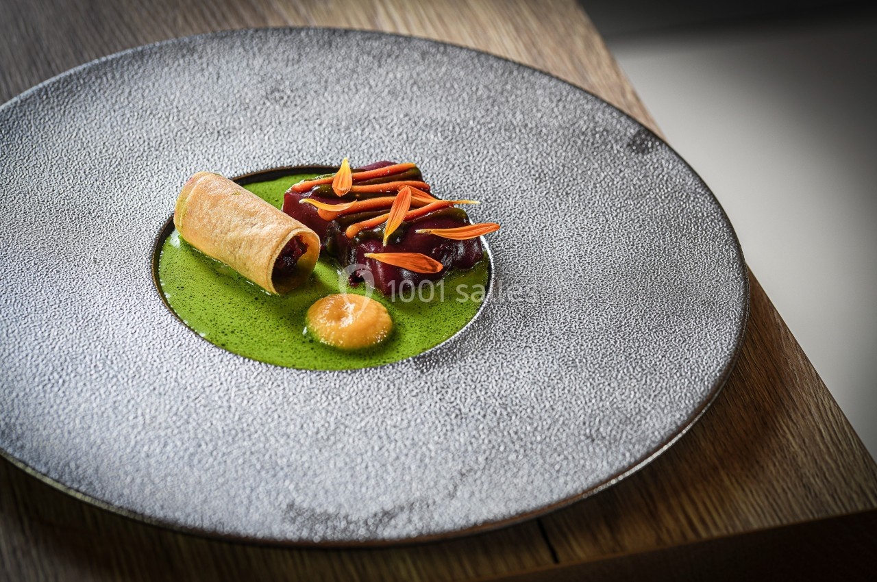 Assiette gastronomique avec un rouleau croustillant, morceaux de viande, sauce verte et garniture colorée.