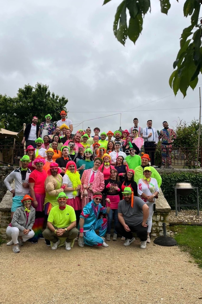 Un grand groupe de personnes en tenues colorées posant à l'extérieur devant un jardin.