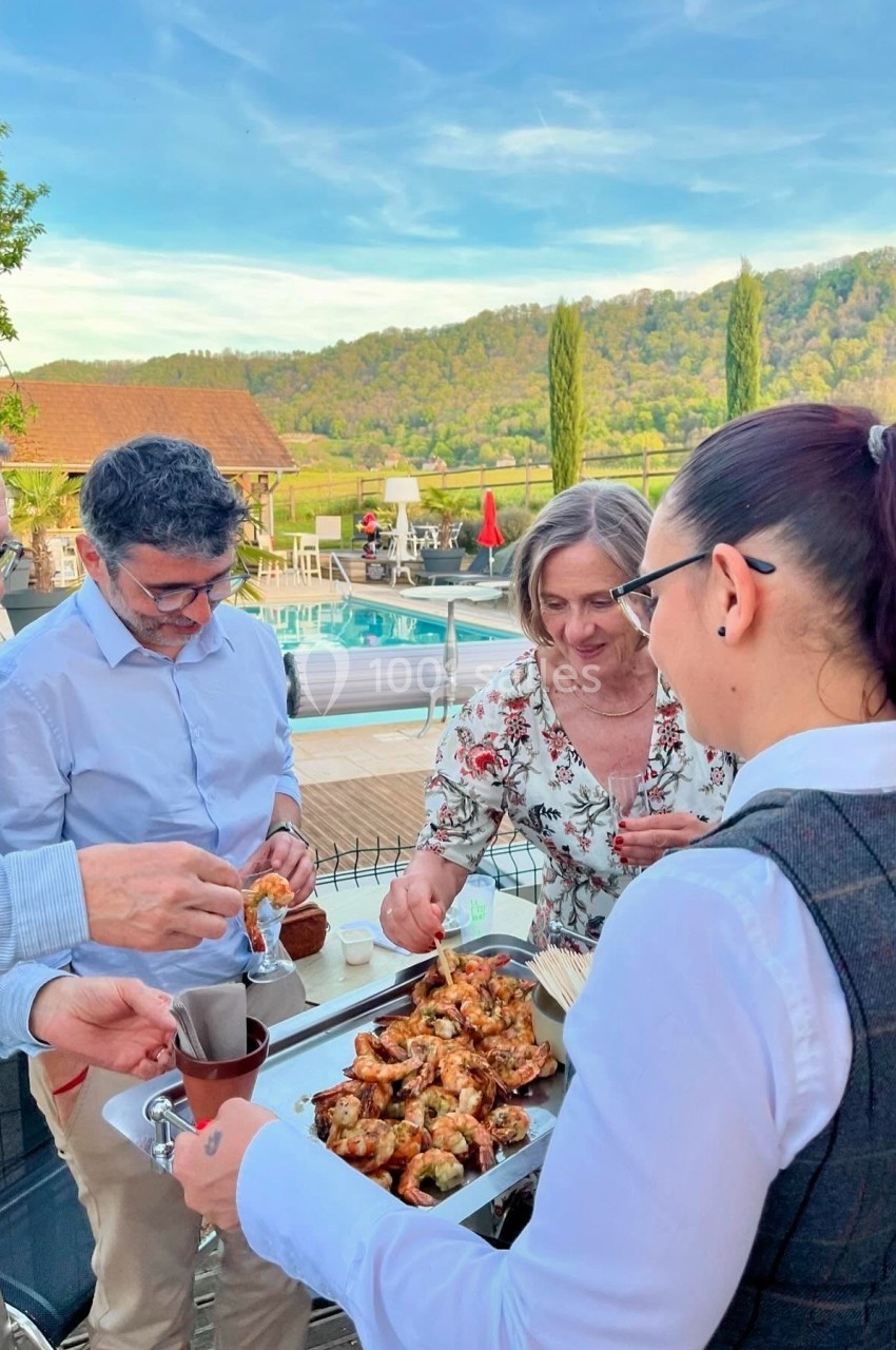 Un groupe de personnes partage des amuse-bouches servis sur un plateau en extérieur, près d'une piscine et d'un paysage…