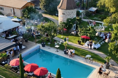 Vue aérienne d'un domaine rural avec des bâtiments, une tente beige, des espaces verts et des participants dispersés.