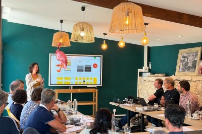 Vue aérienne d'un domaine rural avec des bâtiments, une tente beige, des espaces verts et des participants dispersés.