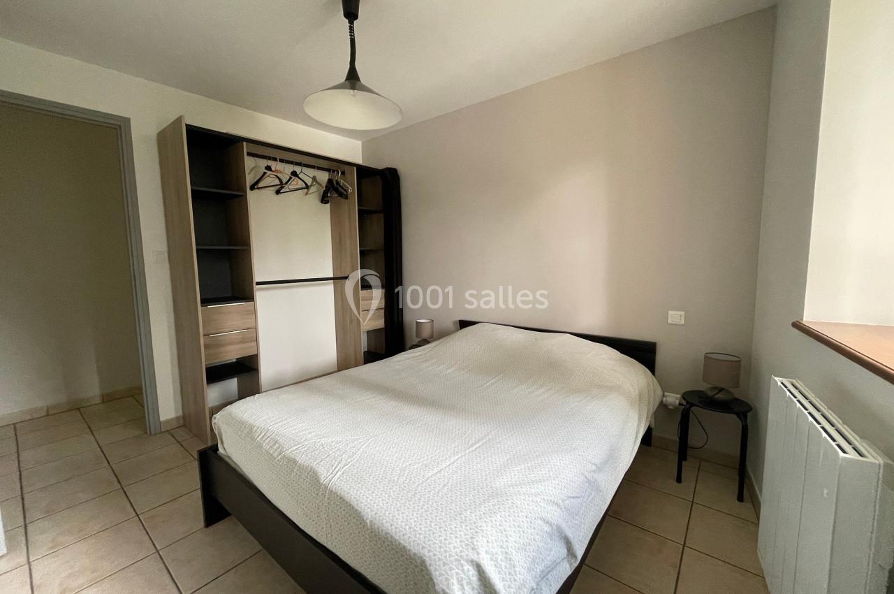 Chambre lumineuse avec lit double, armoire ouverte, table de chevet et sol en carrelage beige.