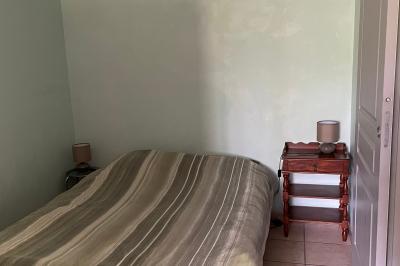 Chambre avec un lit double, draps rayés verts, table de chevet en bois, lampes et sol carrelé beige.