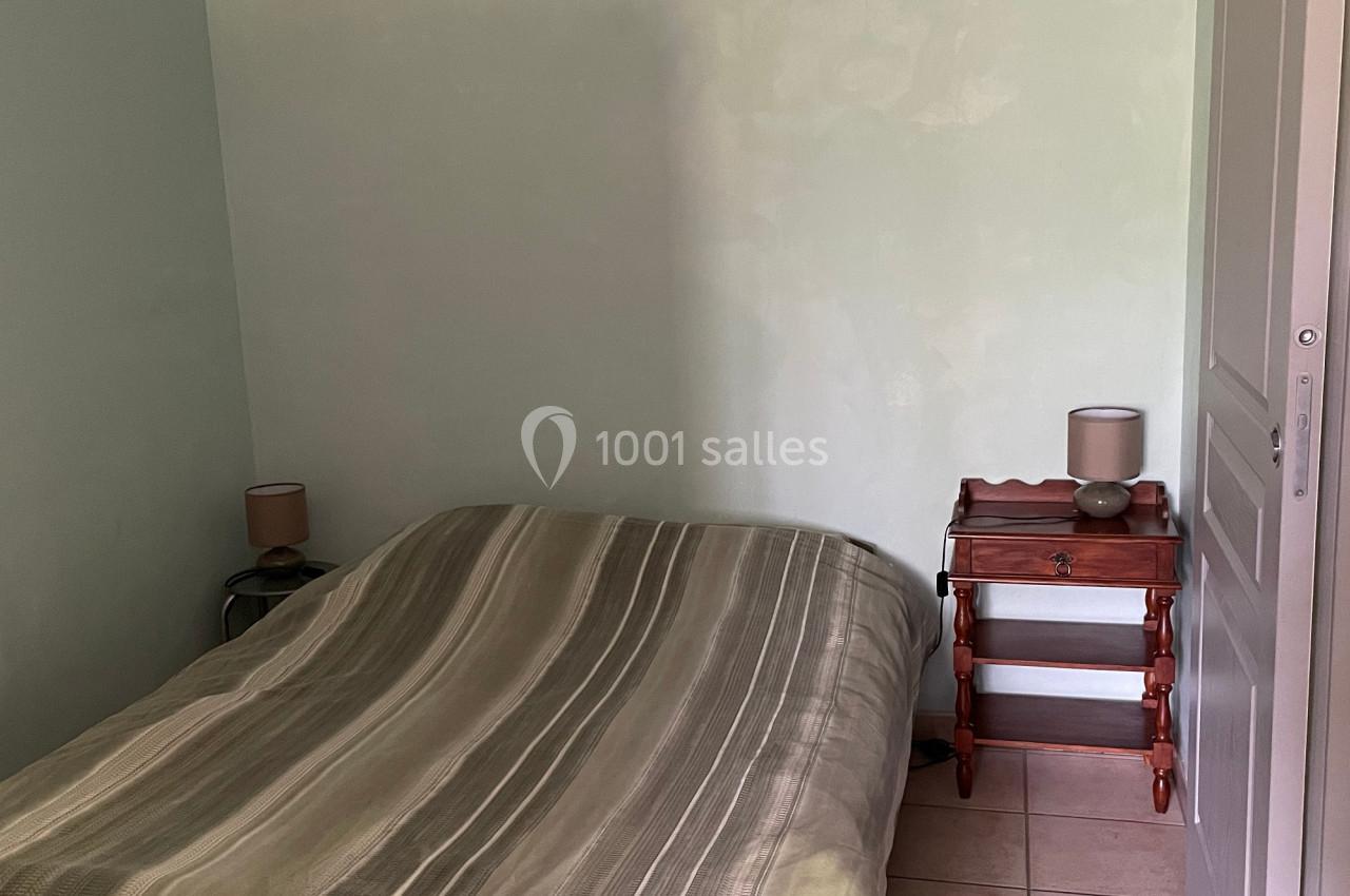 Chambre avec un lit double, draps rayés verts, table de chevet en bois, lampes et sol carrelé beige.