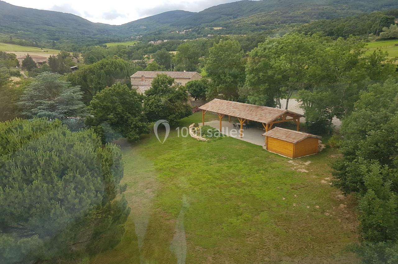 Vue aérienne d'un espace verdoyant avec un abri en bois, des arbres et des collines en arrière-plan.