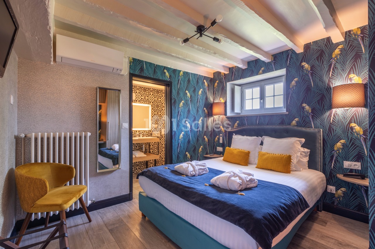 Chambre lumineuse avec lit double, décoration tropicale, plafond avec poutres apparentes et salle de bain attenante.