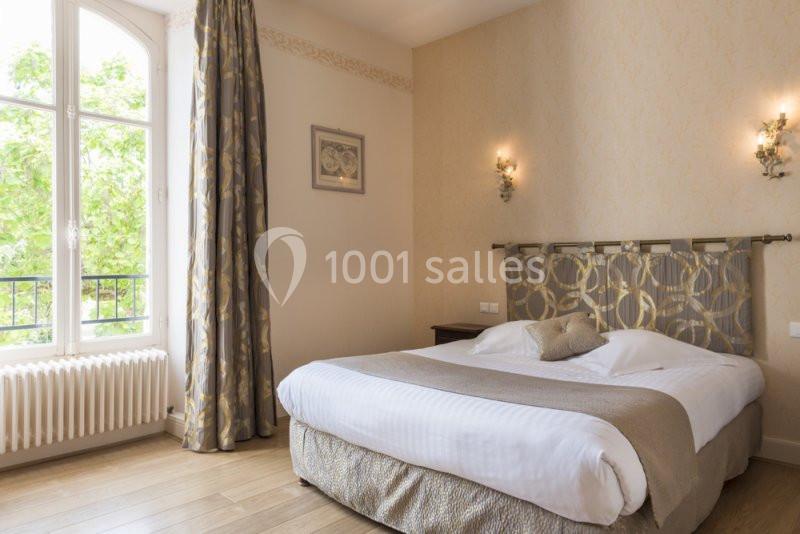 Chambre lumineuse avec un lit double, des murs clairs, des rideaux assortis et une fenêtre donnant sur des arbres.
