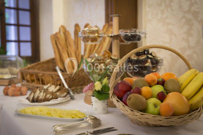 Buffet avec corbeille de fruits, viennoiseries, baguettes, œufs et tranches de pain sur une table dressée.