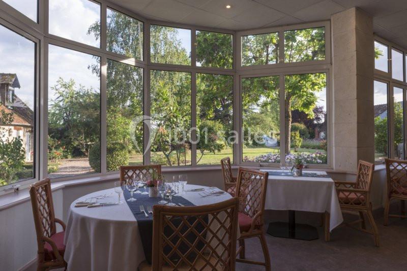 Salle de restaurant lumineuse avec de grandes baies vitrées donnant sur un jardin verdoyant.