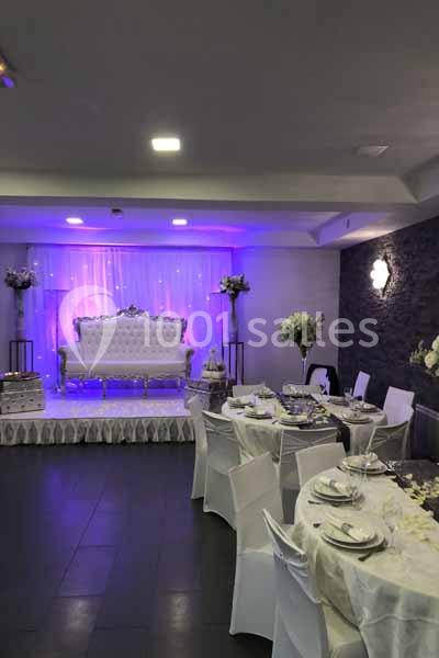 Salle de réception décorée avec des tables dressées, un canapé blanc sur une estrade et un éclairage violet.
