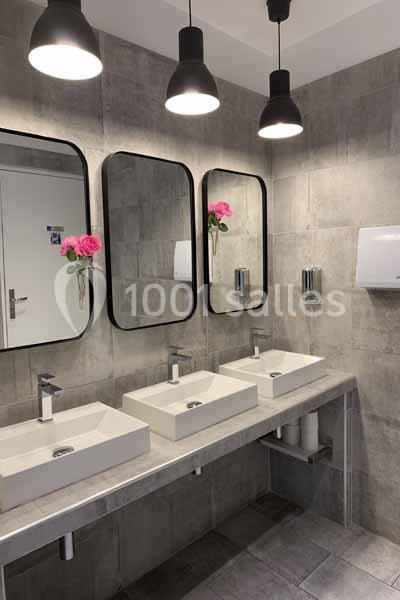 Salle de bain moderne avec trois lavabos, miroirs rectangulaires, éclairage suspendu et roses décoratives.