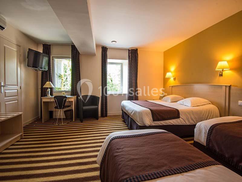 Chambre d'hôtel avec trois lits, bureau, fauteuil, télévision murale et éclairage chaleureux.