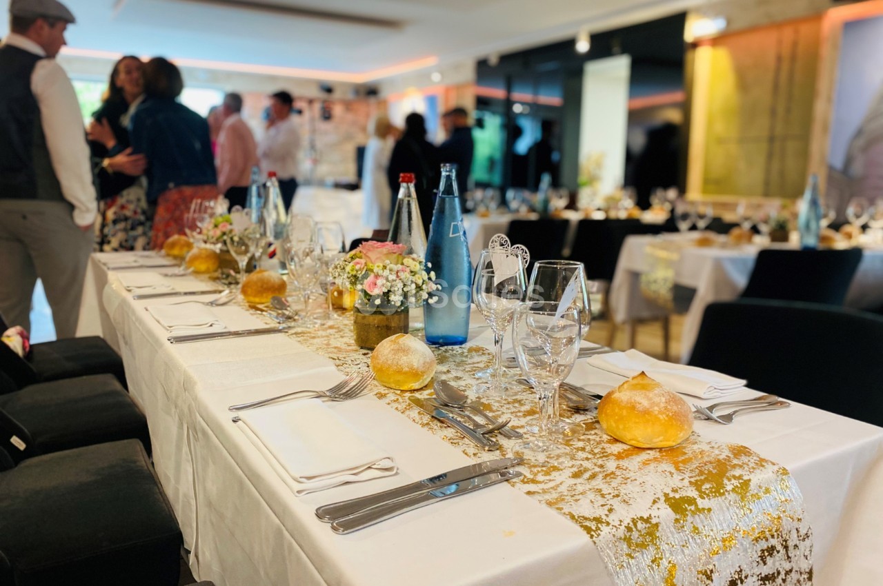 Table élégamment dressée avec nappes blanches, vaisselle, bouteilles d'eau et décoration florale, dans une salle animée.