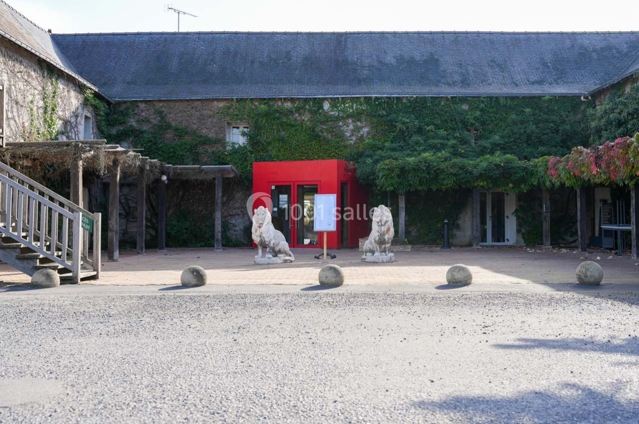 Entrée d'un bâtiment avec une structure rouge, deux statues de lions et des murs recouverts de végétation.