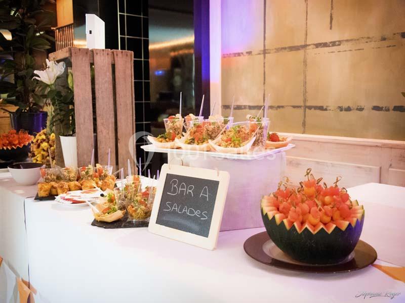 Buffet avec un bar à salades, des verrines colorées et une pastèque sculptée garnie de fruits.