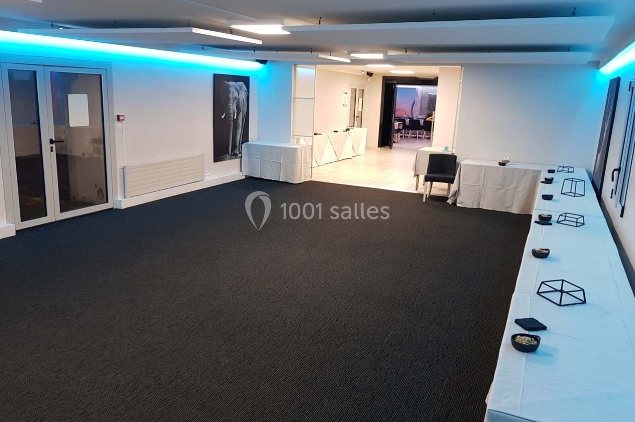 Salle vide avec moquette sombre, tables couvertes de nappes blanches le long des murs et éclairage LED bleu au plafond.