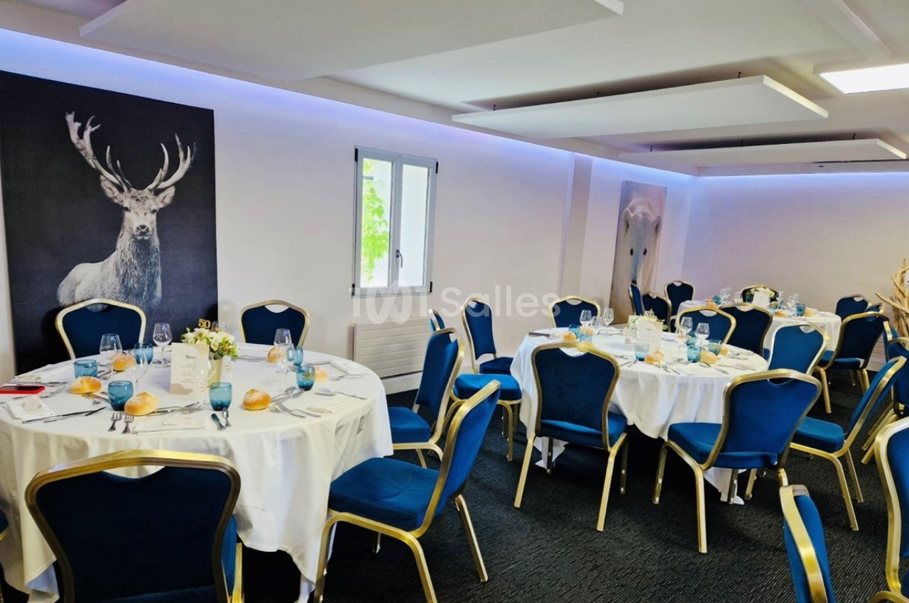 Salle de réception lumineuse avec des tables rondes dressées, des chaises bleues et des tableaux d'animaux sur les murs.