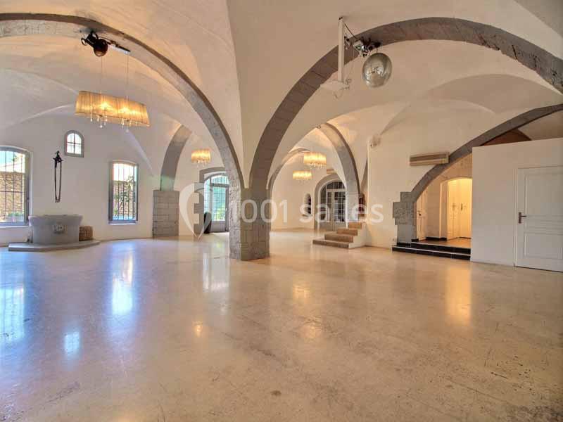 Salle spacieuse avec arches en pierre, sol clair et grandes fenêtres laissant entrer la lumière naturelle.