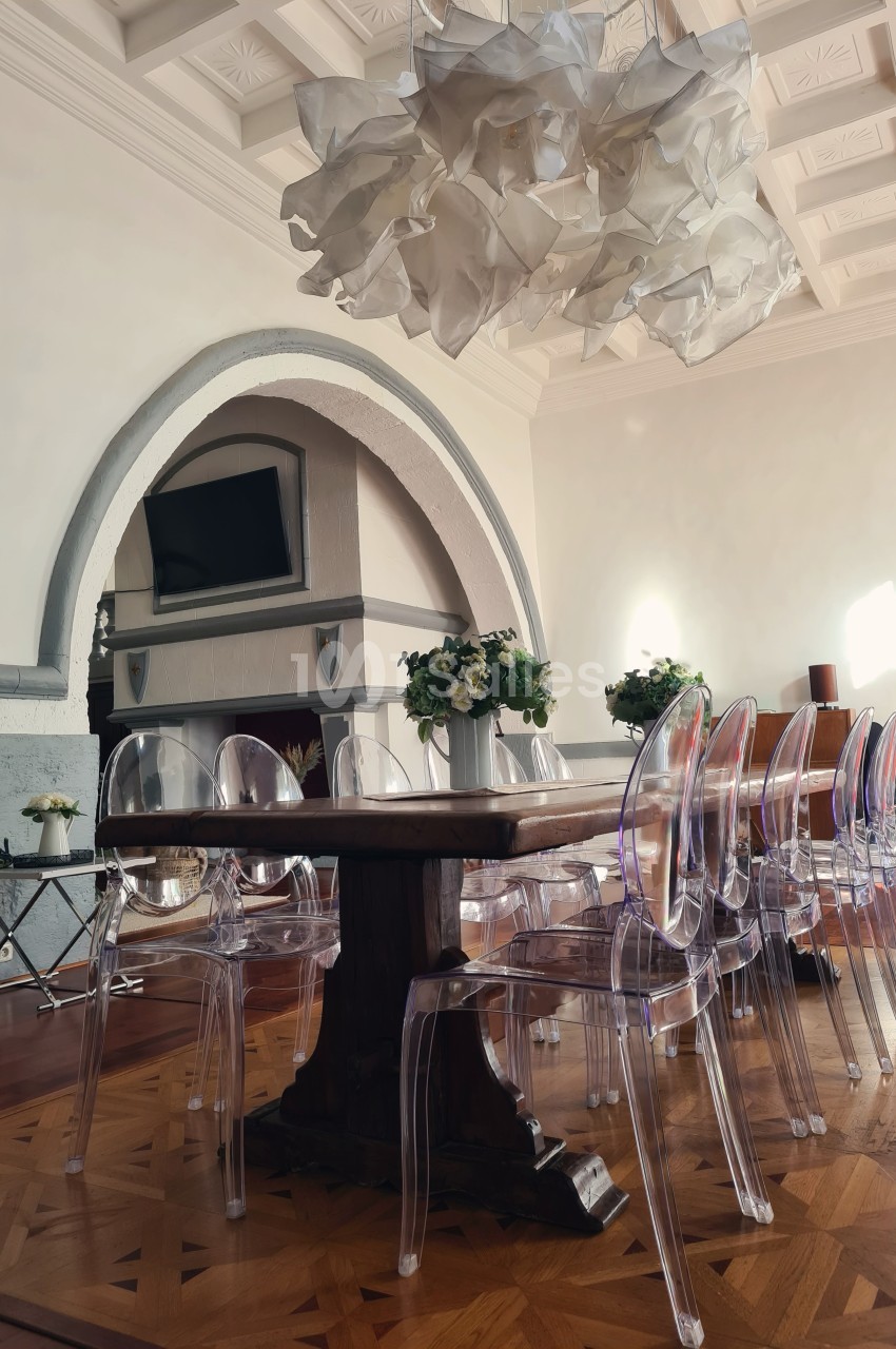 Salle à manger lumineuse avec table en bois, chaises transparentes et lustre design sous un plafond à caissons.