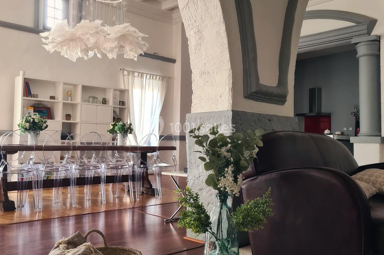 Intérieur lumineux avec salon, fauteuil en cuir, panier en osier, vase fleuri et salle à manger en arrière-plan.