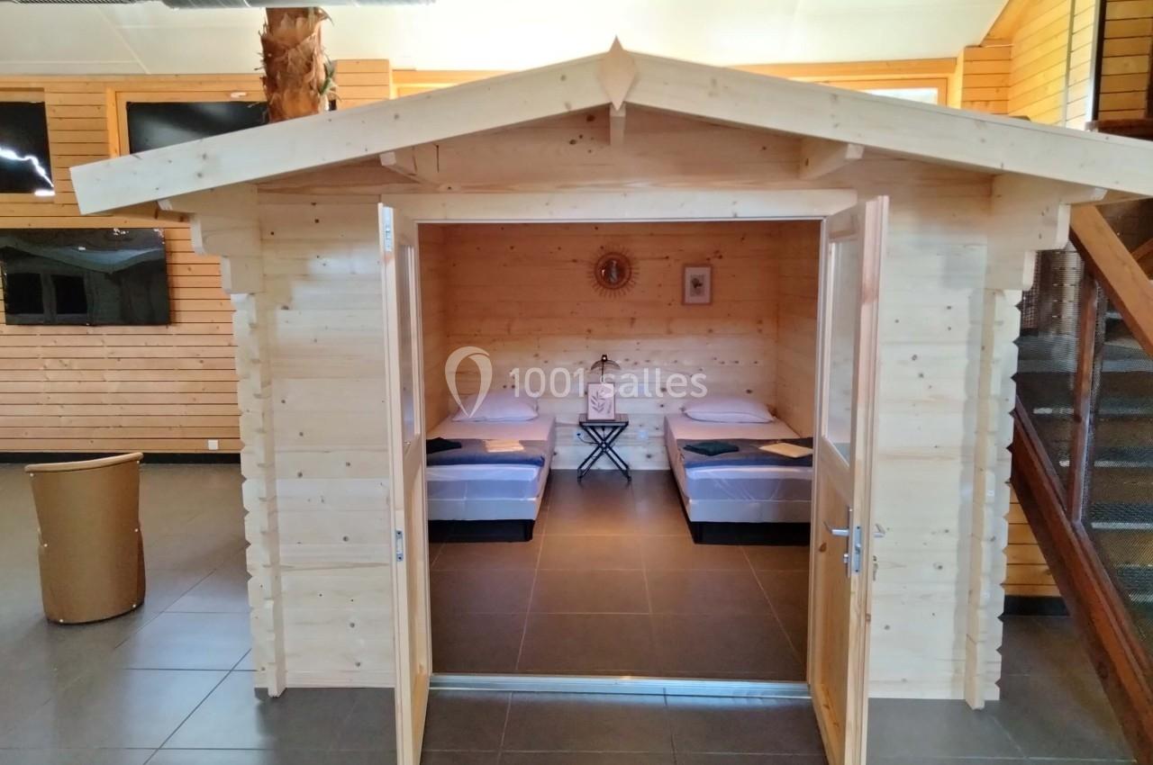 Cabane en bois intérieur avec deux lits simples, située dans un espace moderne avec murs en bois et escalier visible.