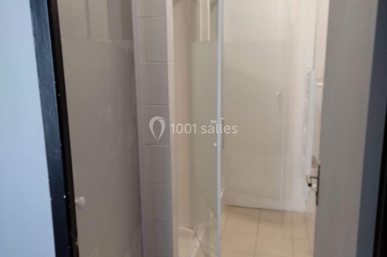 Cabines de douche avec parois vitrées dépolies dans un couloir carrelé éclairé par des spots au plafond.