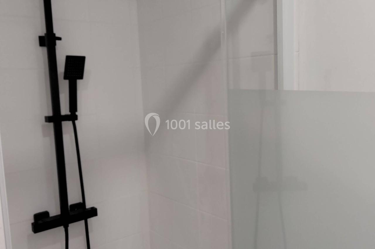 Douche moderne avec paroi vitrée partiellement opaque et colonne de douche noire fixée au mur blanc.